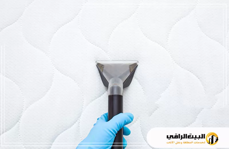 تنظيف المراتب الفيبر بالرياض 0550071994 البيت الراقي شخص يرتدي قفازات زرقاء يقوم بتنظيف مرتبة سرير.